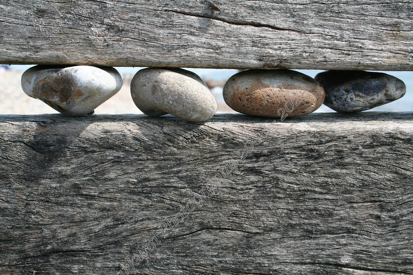 IMG 9799sl 
 pebbles lodged in weather washed grey wood on beach. 
 Keywords: pebbles, beach, wood